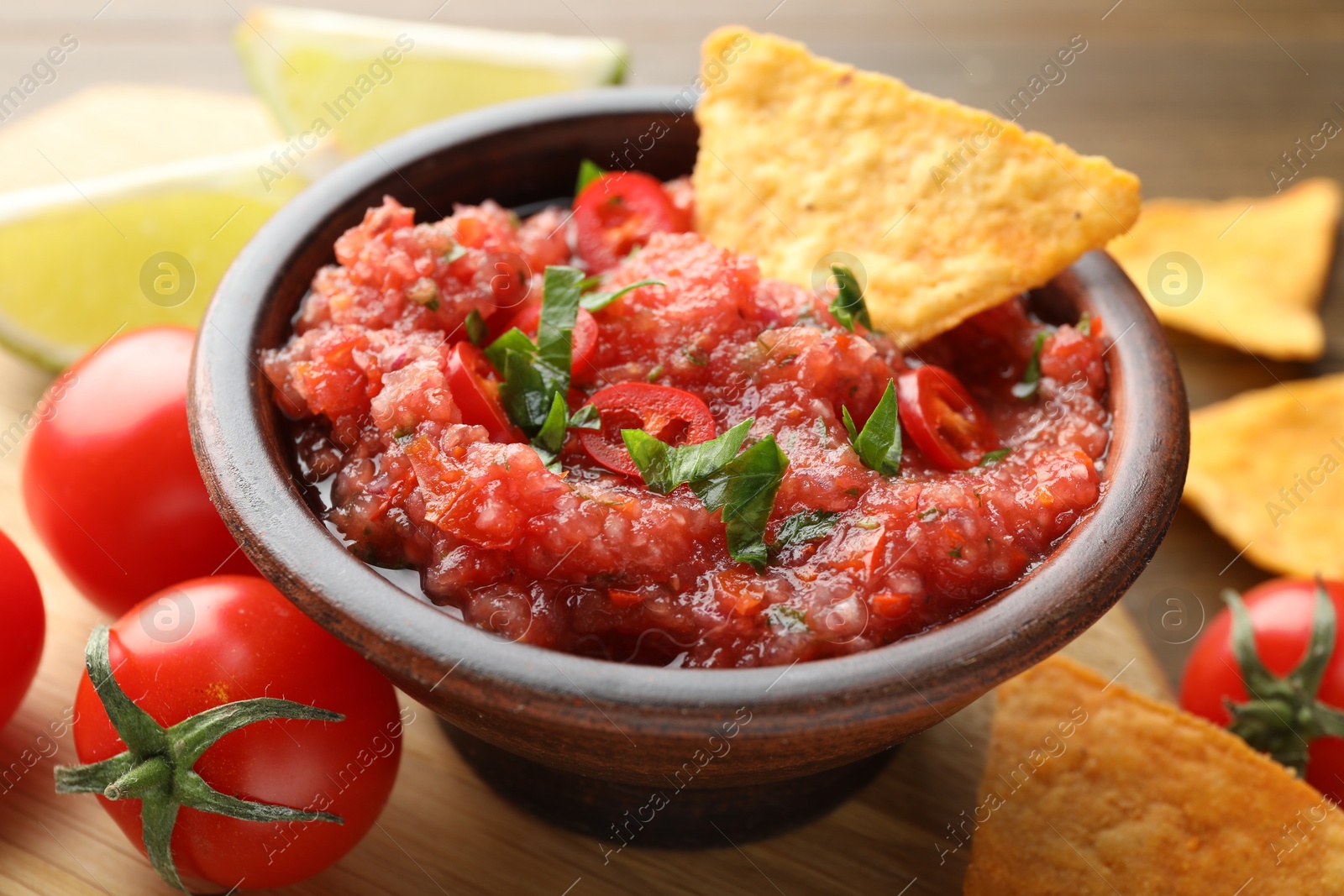 Photo of Spicy salsa in bowl, nachos and tomatoes on table, closeup