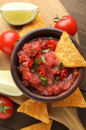 Photo of Spicy salsa in bowl, nachos, tomatoes and lime on wooden table, flat lay