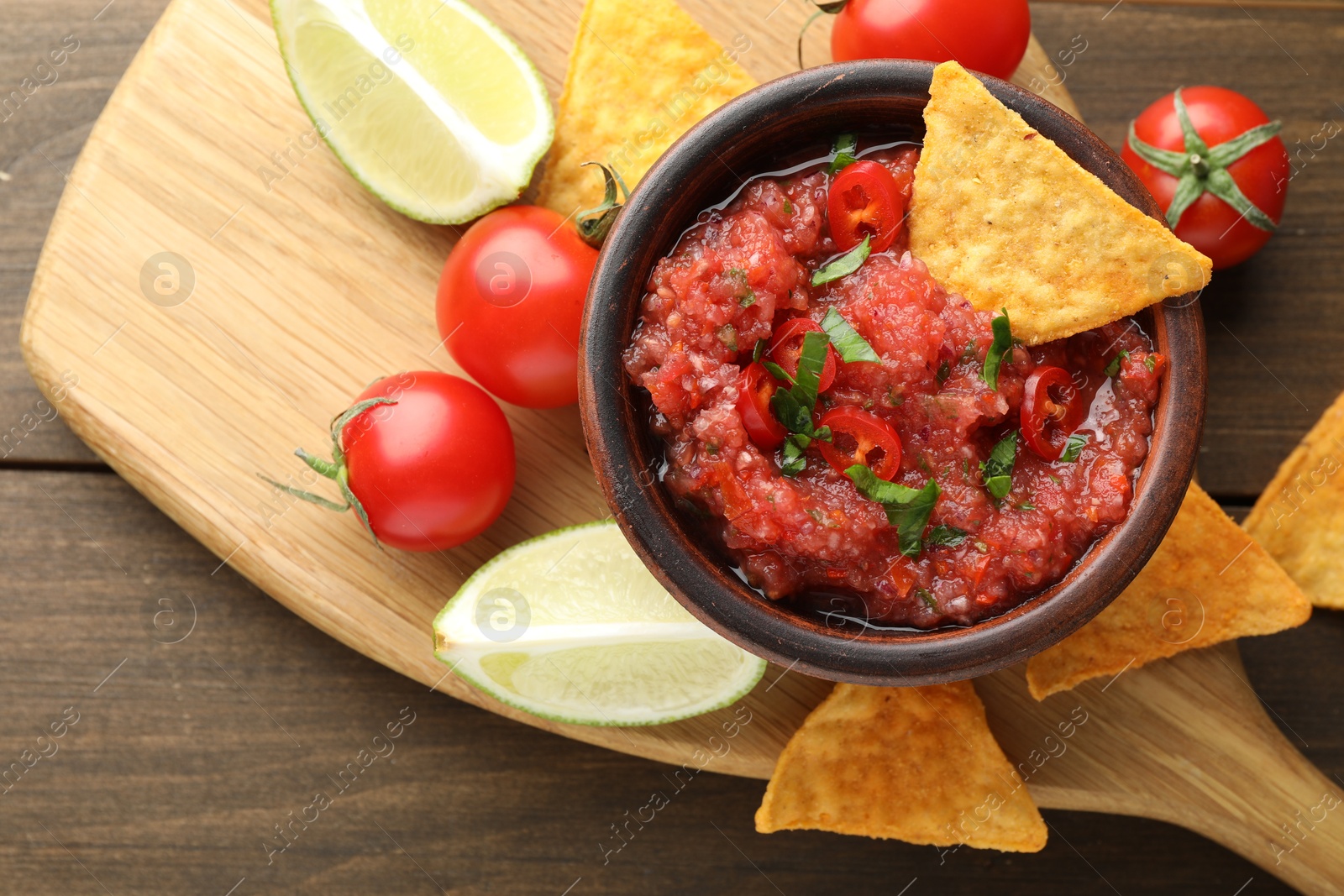 Photo of Spicy salsa in bowl, nachos, tomatoes and lime on wooden table, flat lay