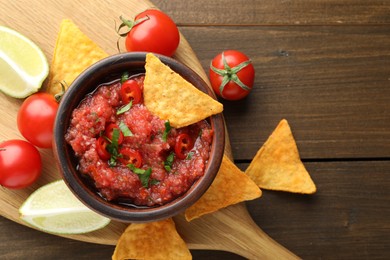 Spicy salsa in bowl, nachos, tomatoes and lime on wooden table, flat lay. Space for text