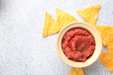 Spicy salsa in bowl and nachos on light grey table, flat lay. Space for text