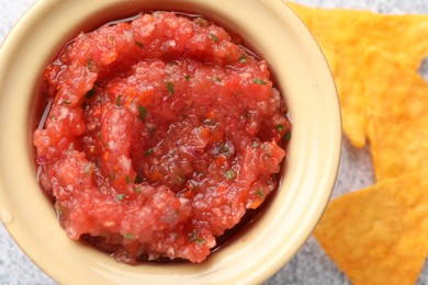 Spicy salsa in bowl and nachos on table, top view