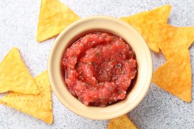 Photo of Spicy salsa in bowl and nachos on light grey table, flat lay