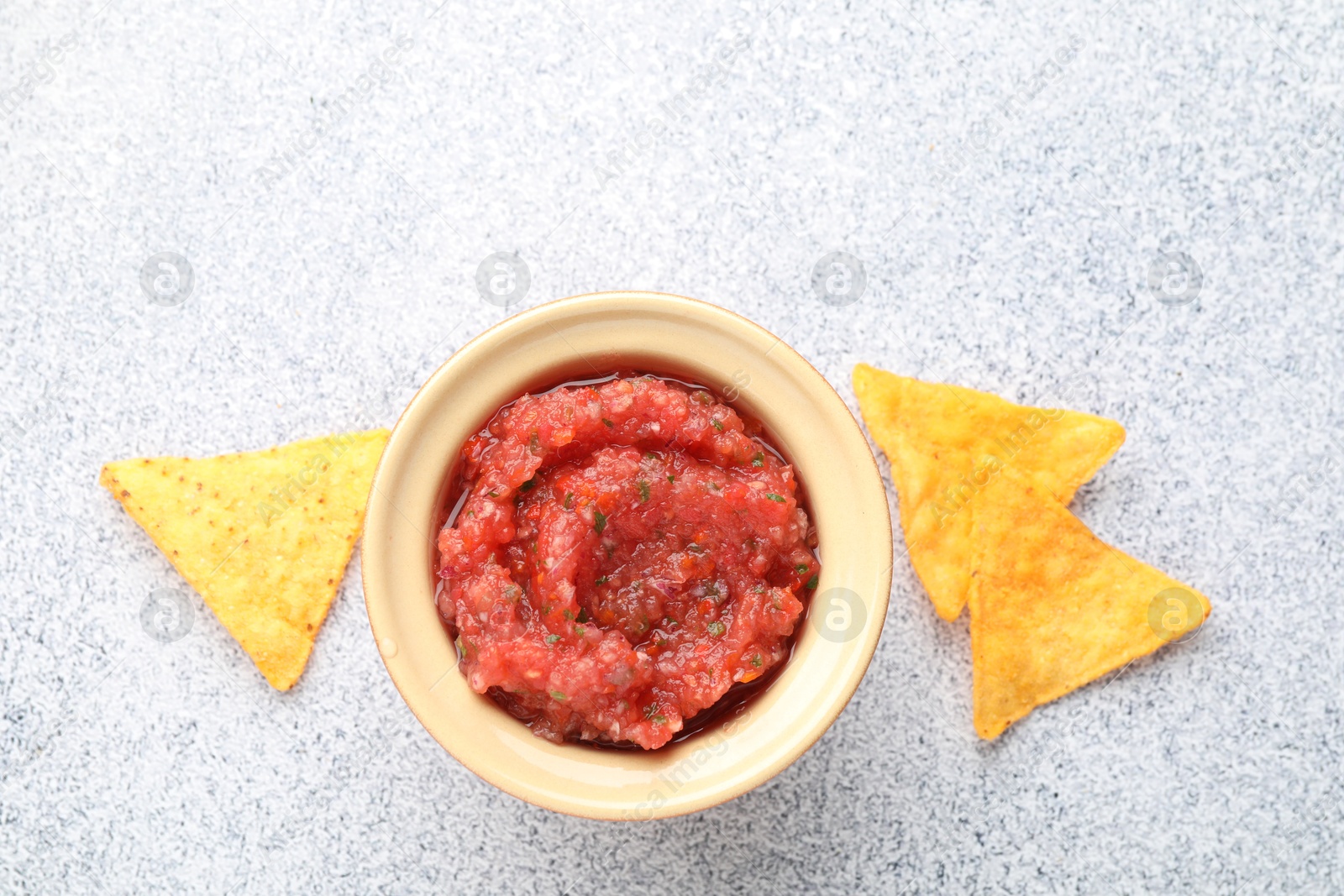 Photo of Spicy salsa in bowl and nachos on light grey table, flat lay