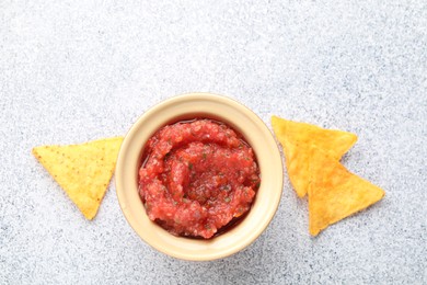 Spicy salsa in bowl and nachos on light grey table, flat lay