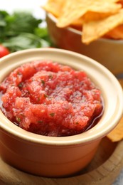 Spicy salsa in bowl and nachos on table, closeup