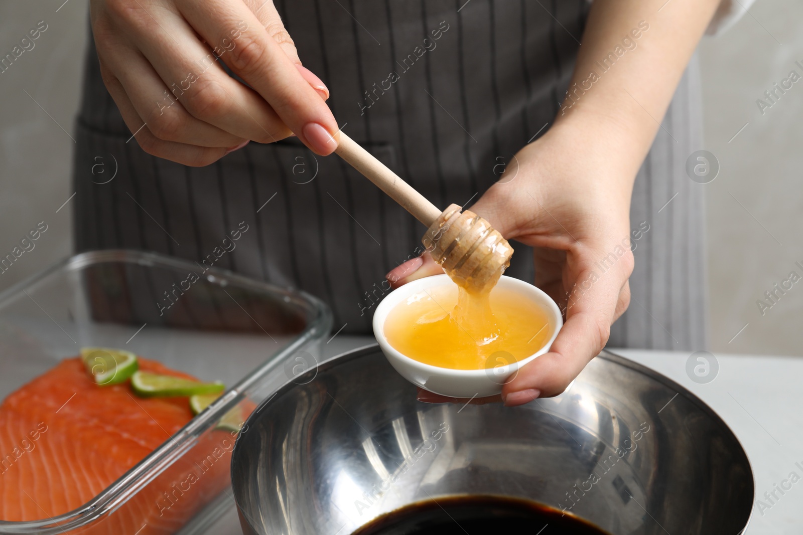 Photo of Woman adding honey into bowl with soy sauce at gray table, closeup