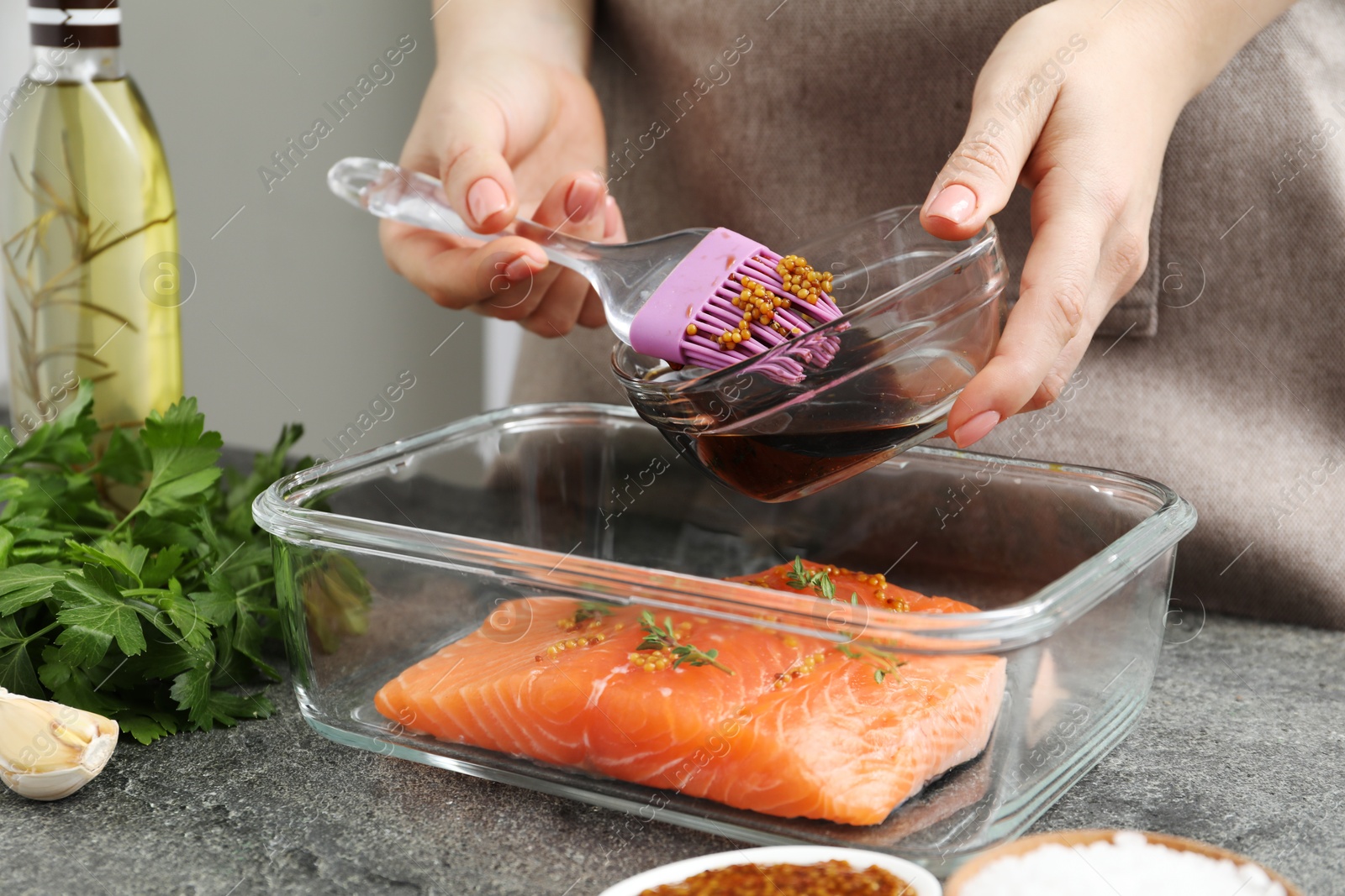 Photo of Woman marinating salmon fillet in dish at gray textured table, closeup