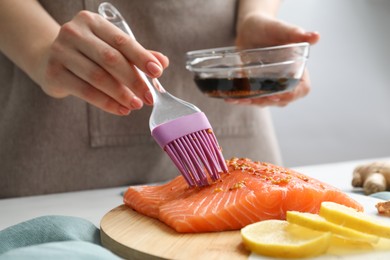 Photo of Woman marinating salmon fillet in dish at table, closeup