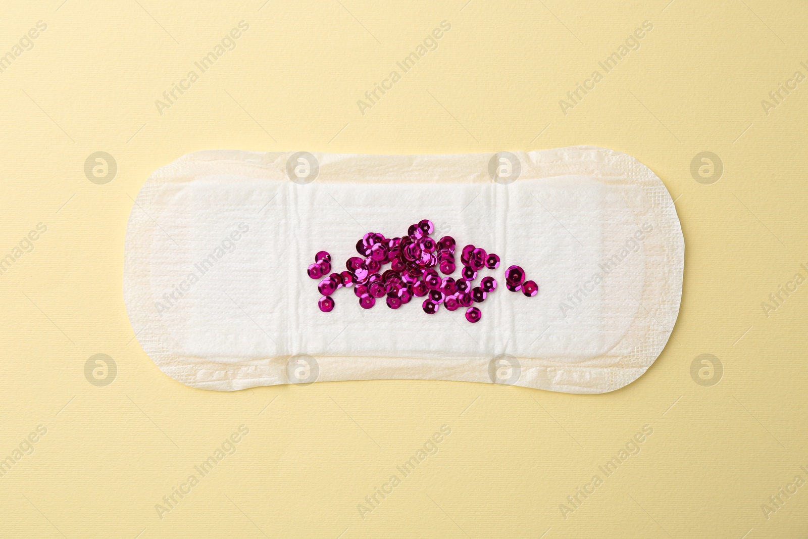 Photo of Menstrual pad with pink sequins on beige background, top view