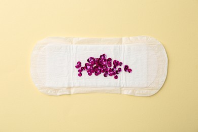 Photo of Menstrual pad with pink sequins on beige background, top view