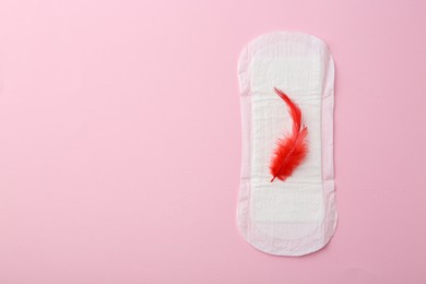 Photo of Menstrual pad with red feather on pink background, top view