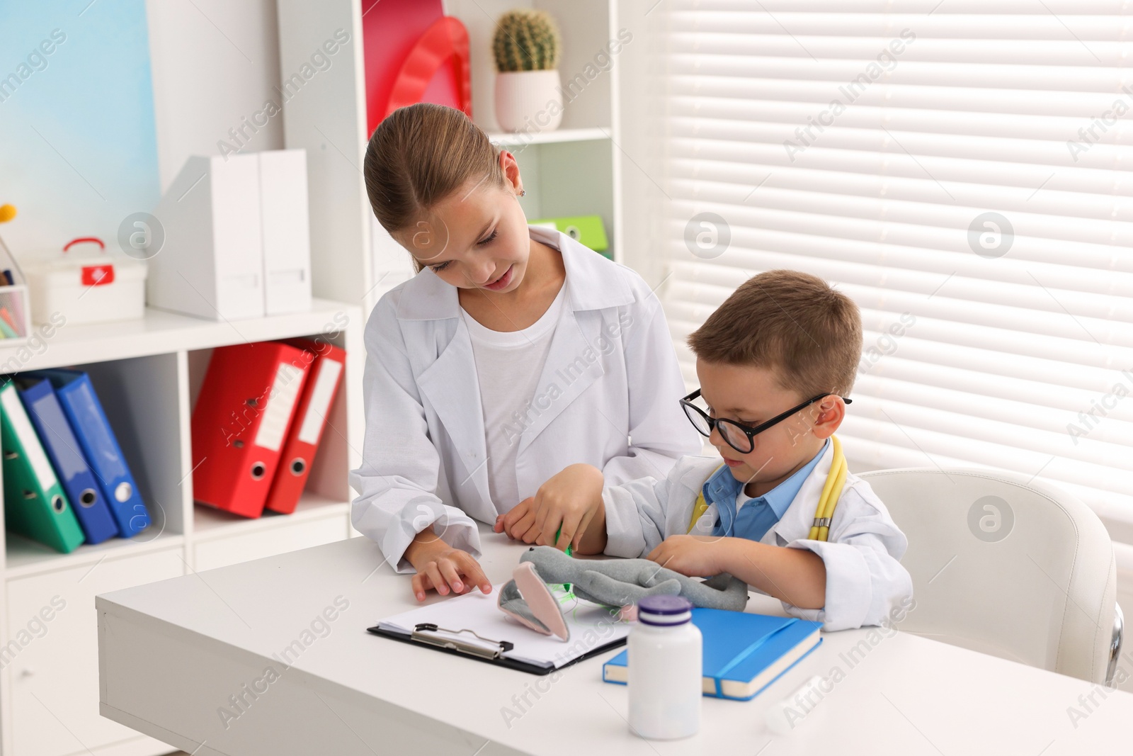 Photo of Little boy and girl pretending to be doctors at white table indoors