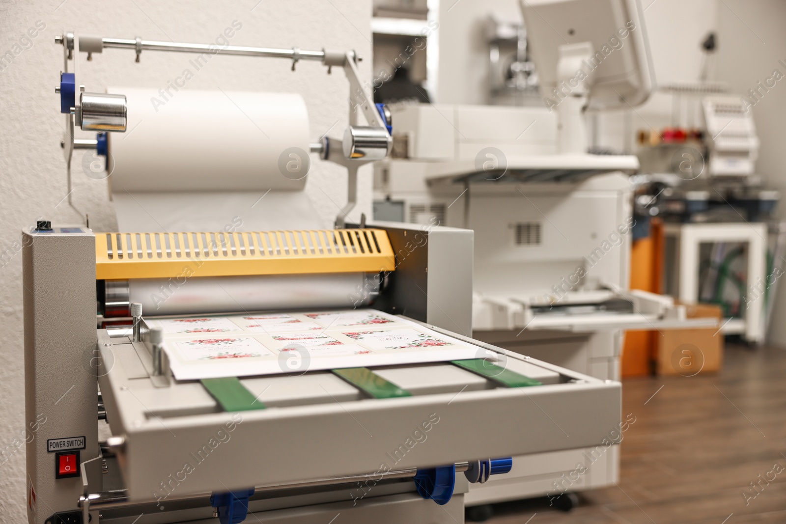 Photo of Modern roll laminator and paper sheet with invitation cards indoors. Printing house