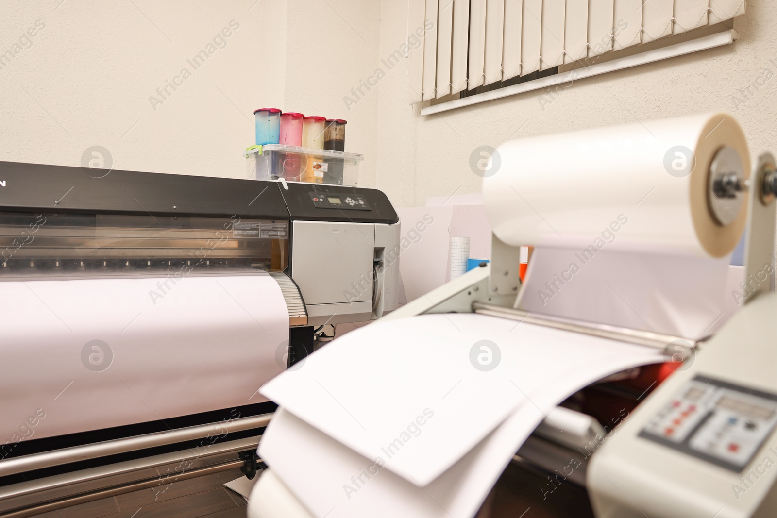 Photo of Wide-format printer and roll laminator with paper indoors, selective focus. Printing house