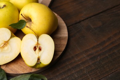 Photo of Fresh ripe yellow apples and green leaves on wooden table, closeup. Space for text