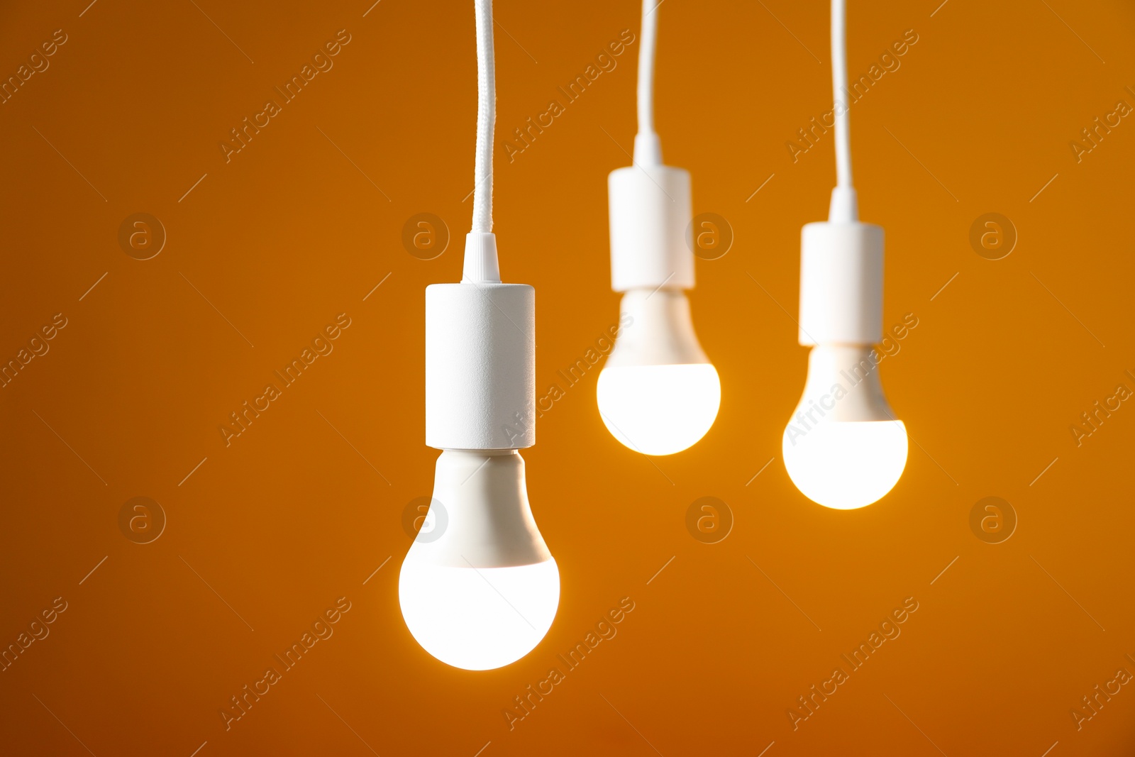 Photo of Light bulbs hanging on cords against orange background, selective focus