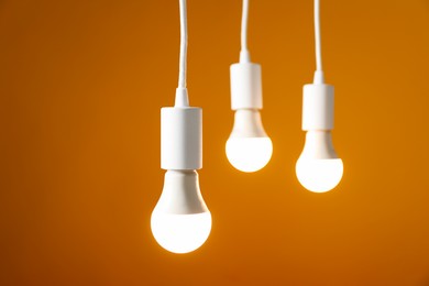 Photo of Light bulbs hanging on cords against orange background, selective focus