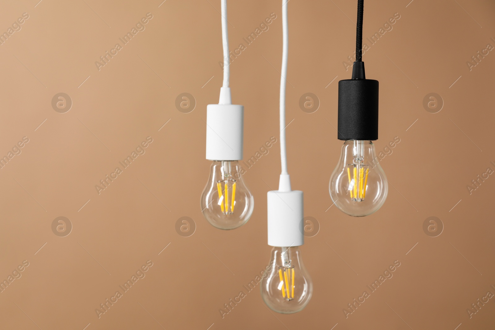 Photo of Light bulbs hanging on cords against beige background, space for text