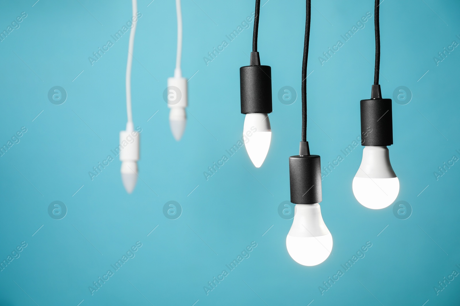 Photo of Light bulbs hanging on cords against blue background, selective focus