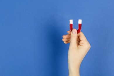 Photo of Woman with horseshoe magnet on blue background, closeup. Space for text