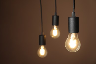 Photo of Light bulbs hanging on cords against brown background, selective focus. Space for text