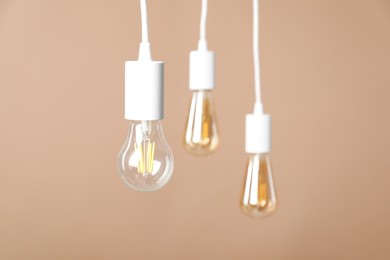 Photo of Light bulbs hanging on cords against beige background, selective focus. Space for text