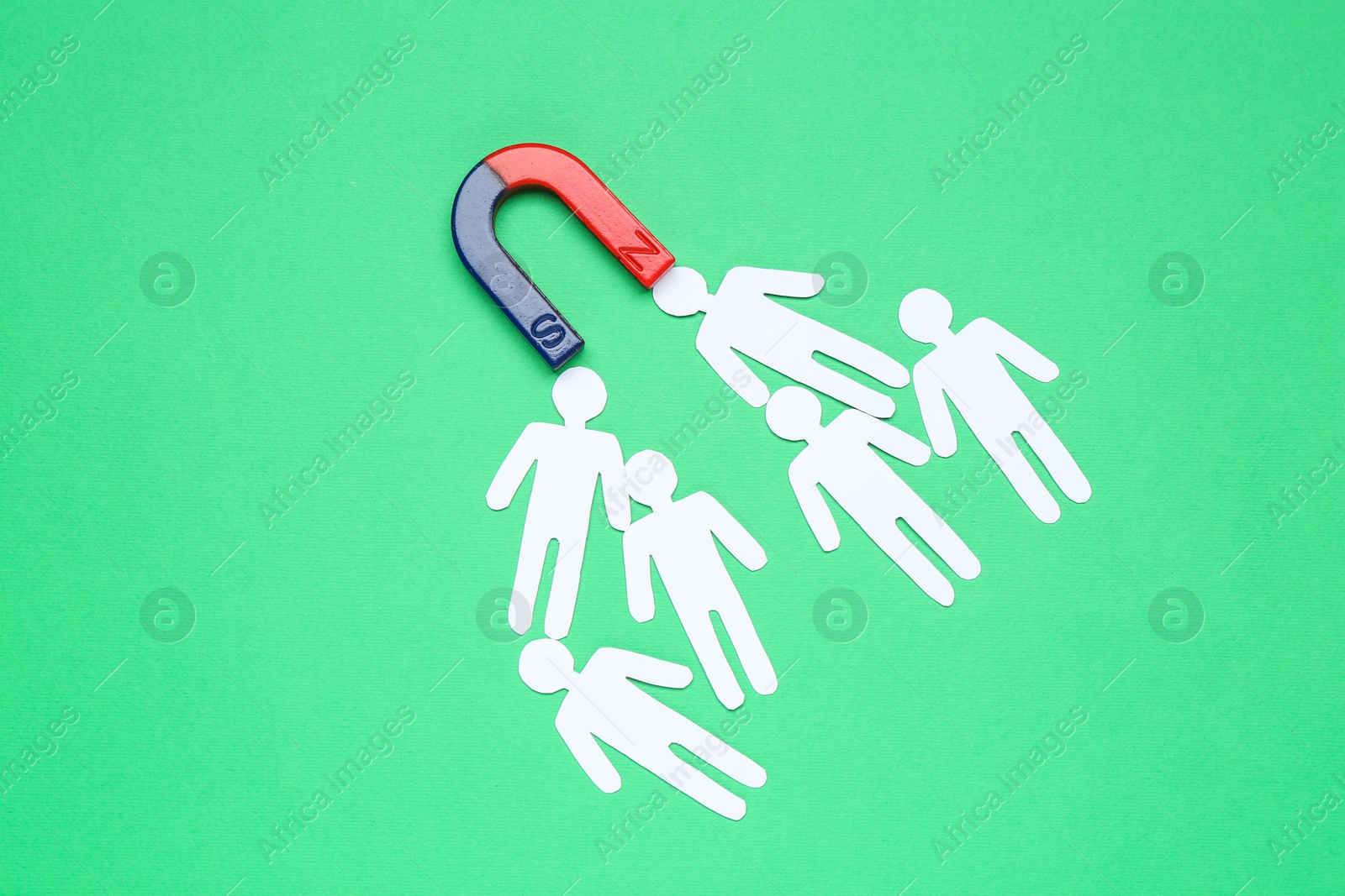 Photo of Magnet attracting paper human figures on green background, flat lay