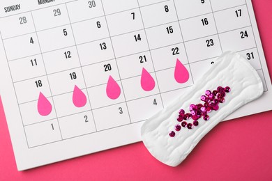 Photo of Calendar with marked dates and menstrual pad with sequins on pink background, top view