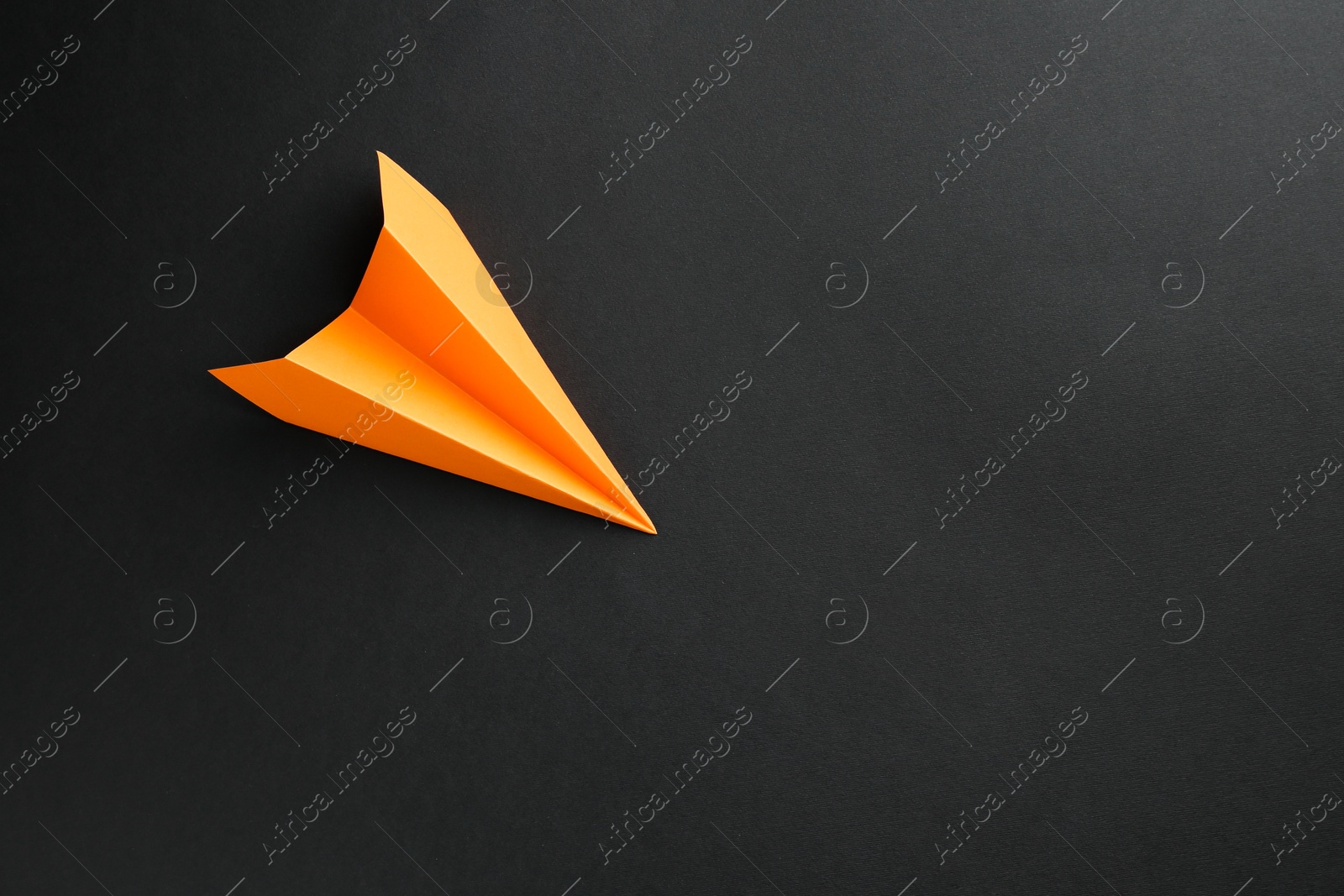 Photo of One handmade orange paper plane on black background, top view. Space for text