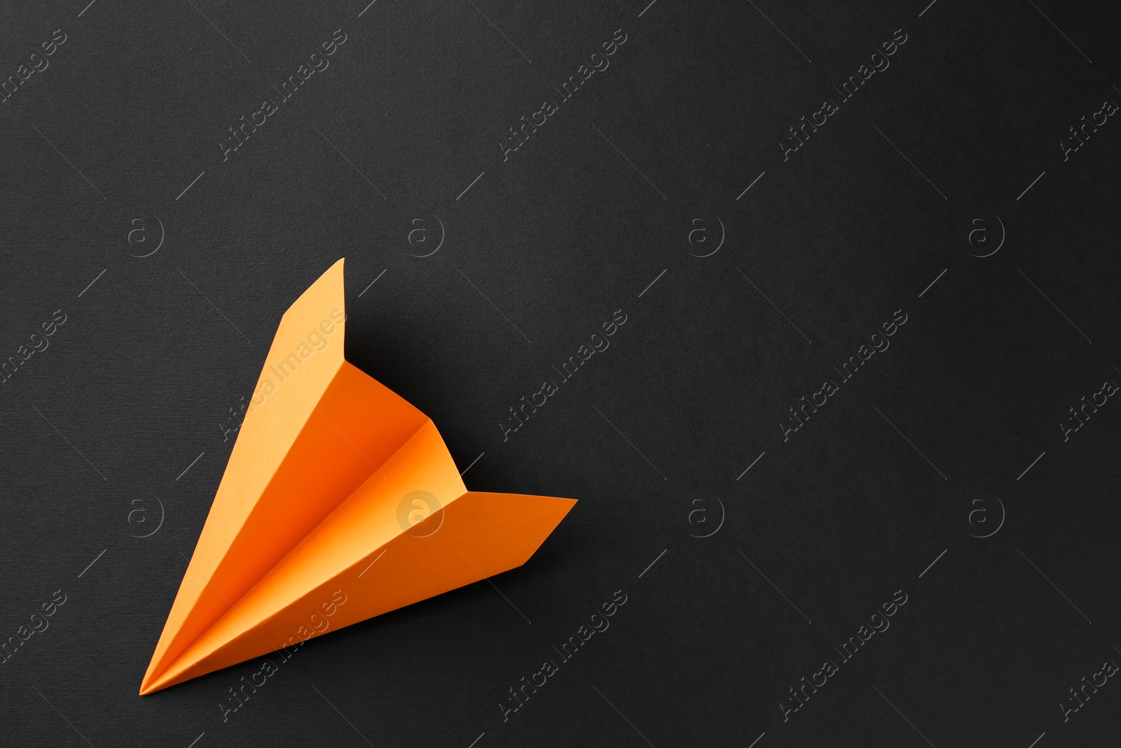 Photo of One handmade orange paper plane on black background, top view. Space for text