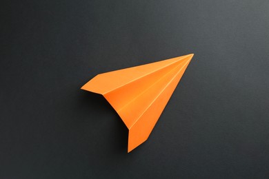 Photo of One handmade orange paper plane on black background, top view