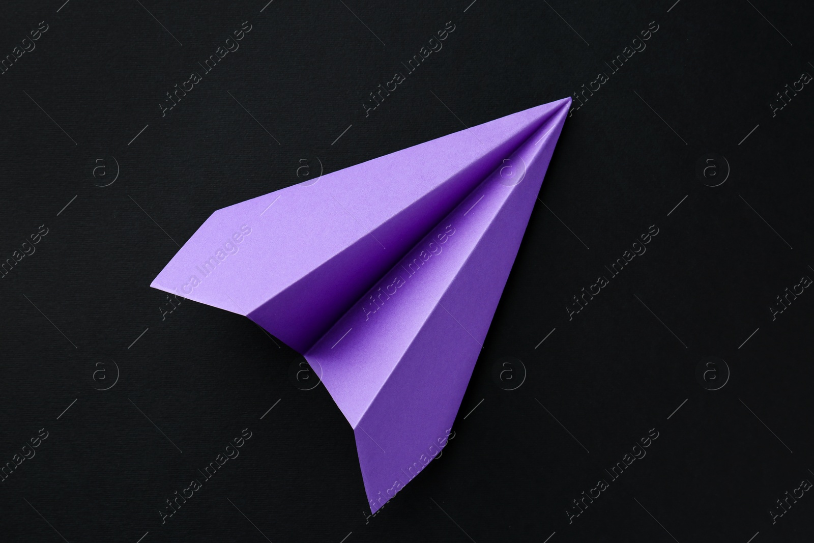 Photo of One handmade violet paper plane on black background, top view