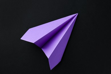 Photo of One handmade violet paper plane on black background, top view