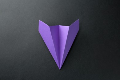 Photo of One handmade violet paper plane on black background, top view