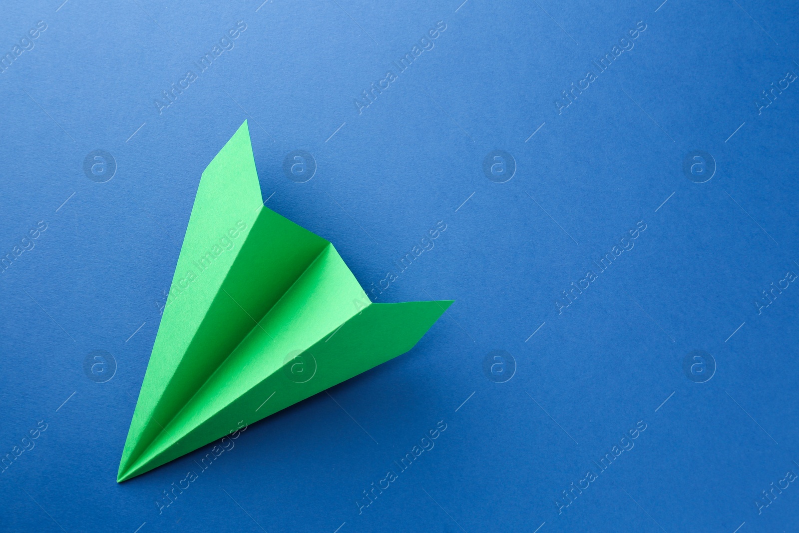 Photo of One handmade green paper plane on blue background, top view. Space for text