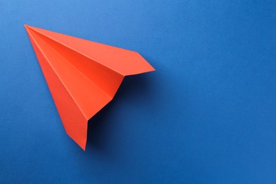 Photo of One handmade coral paper plane on blue background, top view. Space for text