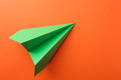 Photo of One handmade green paper plane on orange background, top view. Space for text