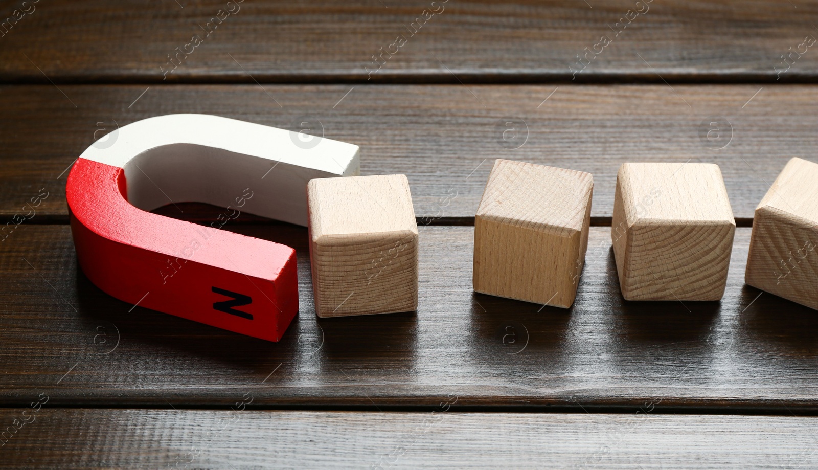 Photo of Magnet attracting cubes on wooden table, closeup