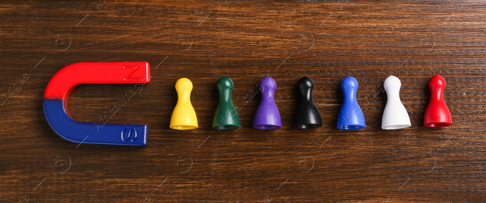 Photo of Magnet attracting colorful game pieces on wooden table, flat lay