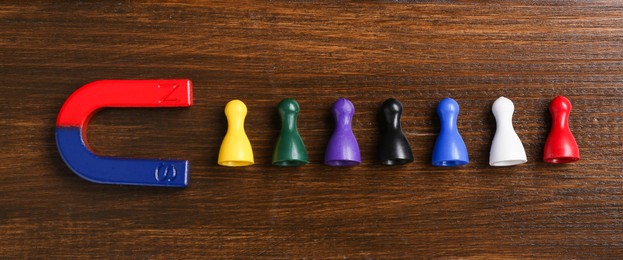 Photo of Magnet attracting colorful game pieces on wooden table, flat lay