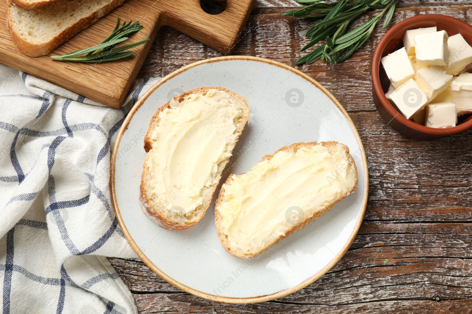 Fresh bread with butter and rosemary on wooden table, flat lay Photo of Fresh bread with butter and rosemary on wooden table, flat lay