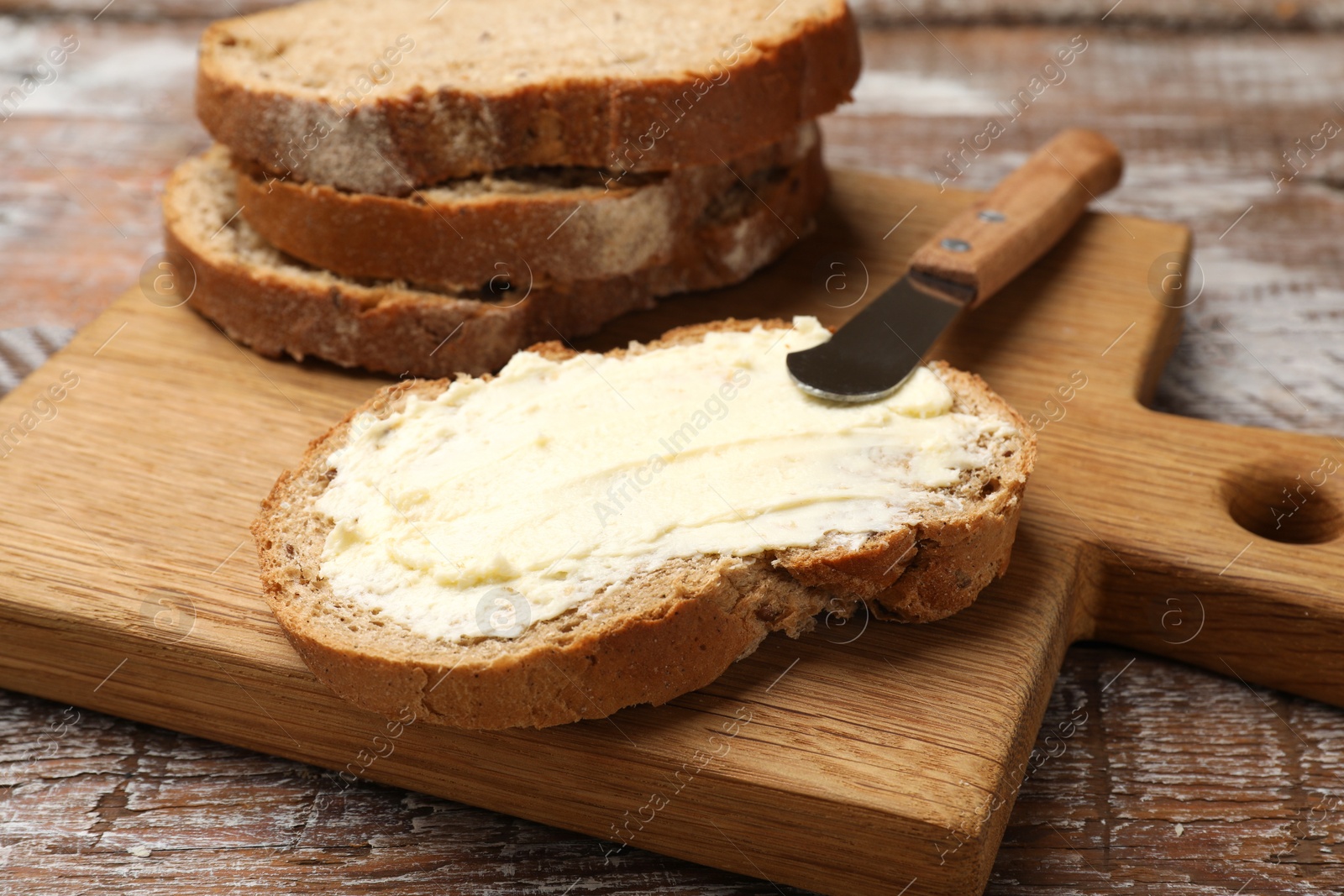 Photo of Fresh bread with butter and knife on wooden table, closeup