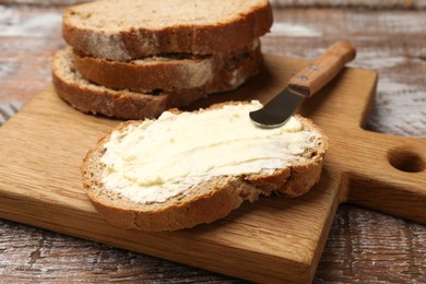 Photo of Fresh bread with butter and knife on wooden table, closeup