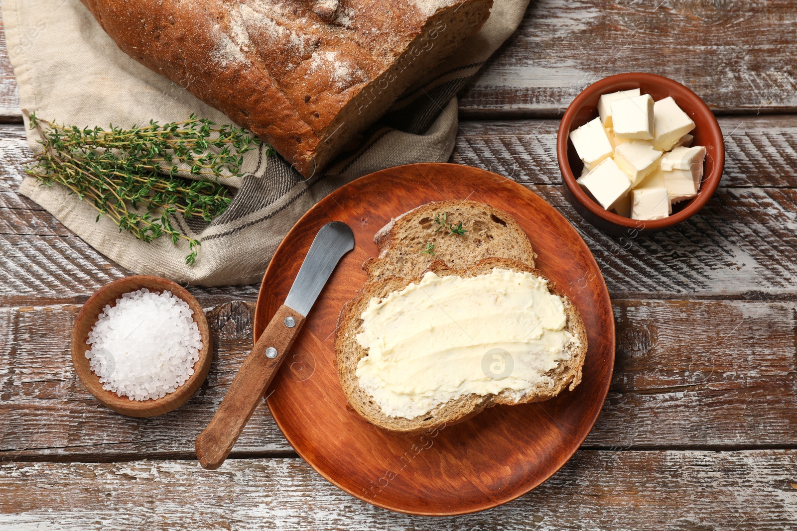 Fresh bread with butter, thyme, salt and knife on wooden table, flat lay Photo of Fresh bread with butter, thyme, salt and knife on wooden table, flat lay