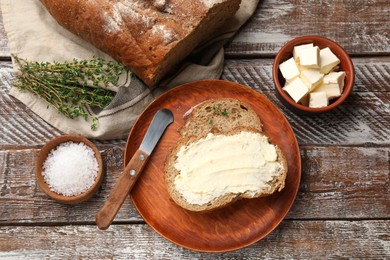 Photo of Fresh bread with butter, thyme, salt and knife on wooden table, flat lay
