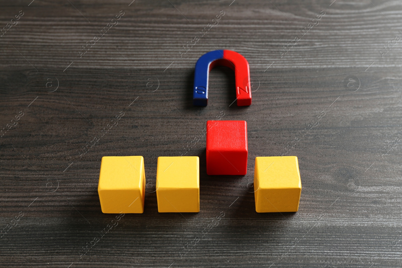 Photo of Magnet attracting red cube among yellow ones on wooden table