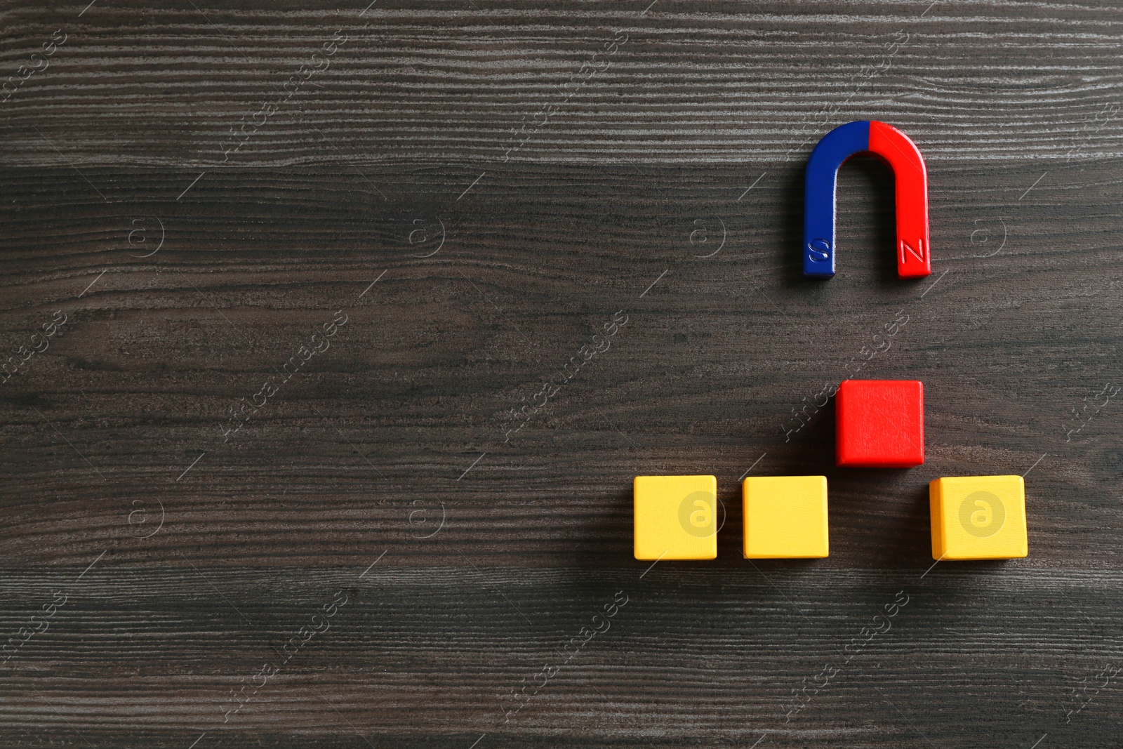 Photo of Magnet attracting red cube among yellow ones on wooden table, flat lay. Space for text