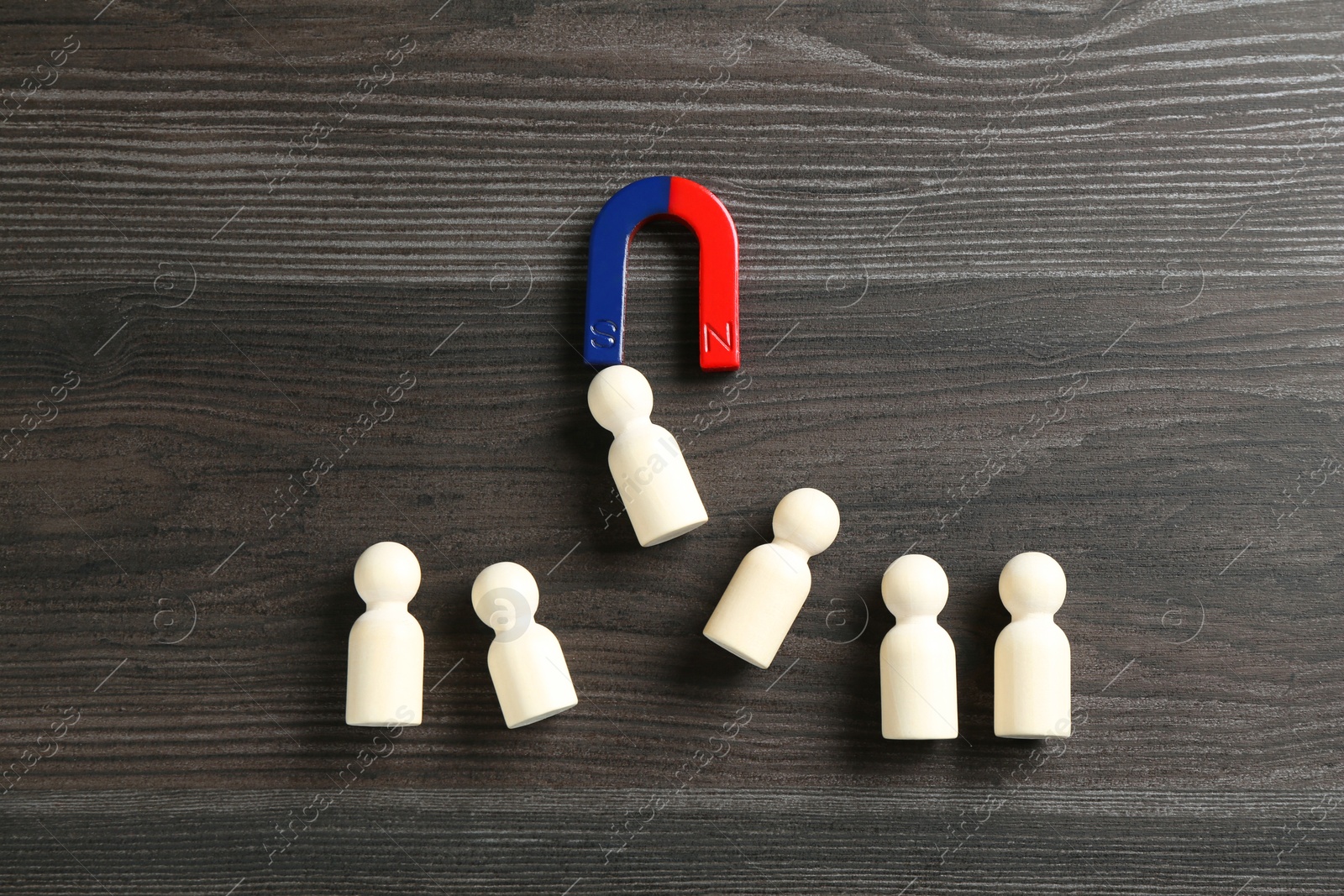 Photo of Magnet attracting human figures on wooden table, flat lay