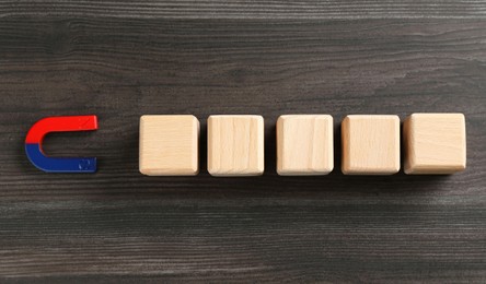 Photo of Magnet attracting cubes on wooden table, flat lay